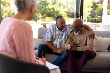 Wall Mural - Multiracial female therapist looking at senior man consoling male friend crying in retirement home