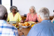 © wavebreak3 - Multiracial senior friends holding hands and saying grace at dining table in nursing home