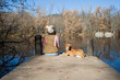 © Sophiaarenasphoto - Mujer adulta sentada junto a un perro mascota en el muelle del lago en el bosque