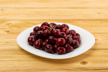 Wall Mural - ripe red cherries in a white plate on a wooden background