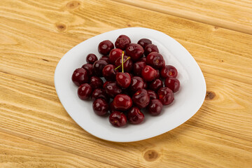 Wall Mural - ripe red cherries in a white plate on a wooden background