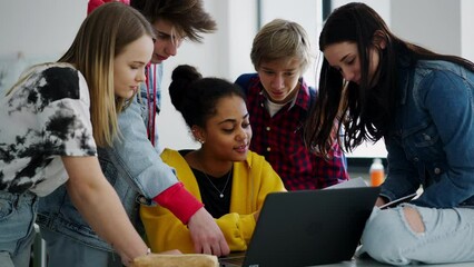 Wall Mural - high school students sitting together at desk and using laptop and talking during break in classroom