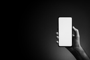 Man's hand holding smartphone with blank screen isolated on dark background