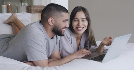 Sticker - Happy young couple bonding and using a laptop at home. Cheerful latin boyfriend and girlfriend talking and browsing online laying on a bed. Husband and wife spending their weekend together