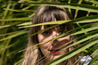 © Manuel - Portrait of young, beautiful, blonde woman looking through the leaves of a green palm tree. Concept beauty, nature, spring, summer, travel.