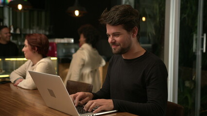 Young entrepreneur working at night in front of laptop inside cafe. Freelance worker using computer at coffee shop