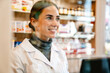 © Drobot Dean - White apothecary wearing lab coat smiling while working in pharmacy