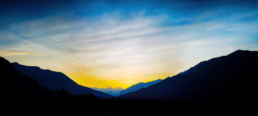 Wall Mural - Mountain landscape panorama background - Sunrise or sunset with silhouette of mountains alps and orange sky..