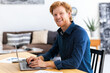 © kucherav - Portrait of confident entrepreneur or small business owner in a modern office or coworking space Successful young businessman is working using laptop sitting workplace Looking at the camera and smile
