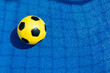 © vejaa - Sports court background. Light blue field rubber ground with shadow from football goal net and yellow soccer ball on sunny day outdoors. Top view