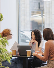 Wall Mural - three female colleagues or students are working on a laptop and discussing a project or creative term paper. three female friends in coworking work online in an intranet or video chat for negotiations