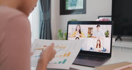 Wall Mural - Young Asia businesswoman using laptop talk to colleagues about plan in video call meeting while work from home at living room. Self-isolation, social distancing, quarantine for coronavirus prevention.