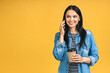 Photo of cheerful cute beautiful young woman talking by mobile phone isolated over yellow wall background.