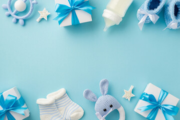 Baby accessories concept. Top view photo of gift boxes teether knitted bunny rattle toy socks booties milk bottle and stars on isolated pastel blue background with empty space