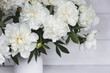 Beautiful white bouquet of peonies in a white vase on a white wooden background. Close-up. Flowers and buds.