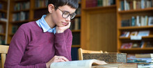 Young Woman Wearing Reading Glasses Reading Book In The Library