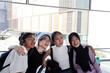 © oqba - Four young attractive Asian group woman friends colleagues students talk walk discuss mingle outdoors backpack handphone outdoor notebook urban building cityscape look show point happy