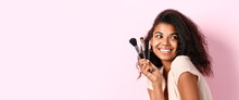 Beautiful Young African-American Woman With Makeup Brushes On Pink Background With Space For Text