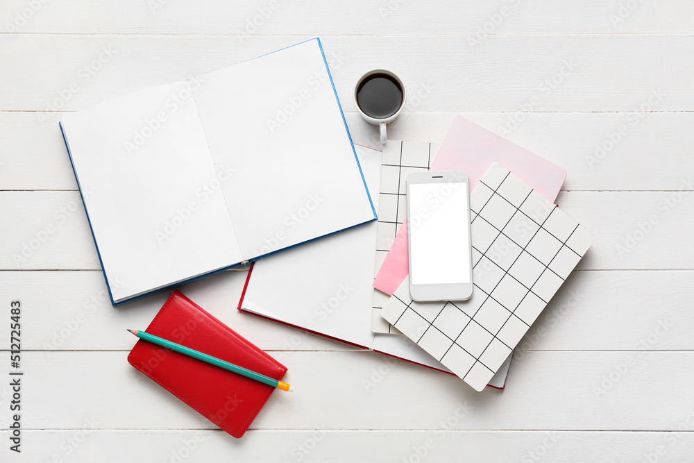 Composition with mobile phone, cup of coffee and notebooks on light wooden background