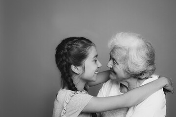 Wall Mural - Cute girl hugging her grandmother on grey background. Black and white photography