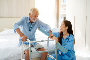 Care worker helping elderly man get out of bed and walk around the room.