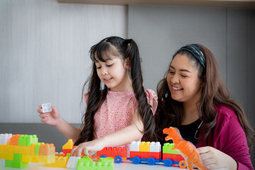 Asian family mother and little asian girl smiling playing with toy build blocks at home. 