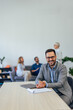 © bnenin - The man sitting at the office, smiling at the camera, colleagues sitting in the background.