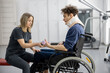 Rehabilitation specialist helps a guy to do exercises for recovery from injury, who is sitting in a wheelchair with a corset around his neck. Concept of physical therapy for people with disabilities