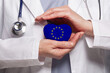 © millaf (Nemchinova) - EU doctor holding heart with flag of European Union background. Healthcare, charity, insurance and medicine concept