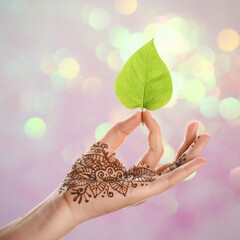 Wall Mural - Woman with henna tattoo on palm holding green leaf against blurred lights, bokeh effect