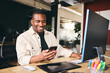 © Southworks - Young Black Male Advertising Marketing Or Design Creative In Modern Office Sitting At Desk Using Mobile Phone