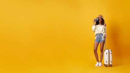 Young pretty african woman tourist smiling holding luggage with camera in hand isolated on yellow background.