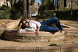 © Manuel - Young and beautiful South American woman in white shirt, jeans and sunglasses on vacation in Europe lying next to a water fountain. Concept beauty, fashion, vacation, travel, water.