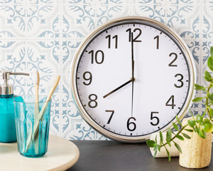 Bathroom. Set with bottle of soap, glass with two teeth brush, clock and home plant on a marble table and tile wall. Cozy morning. Soft focus style image