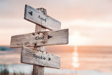 And God Spoke Text Quote On Wooden Crossroad Signpost Outdoors On Beach With Pink Pastel Sunset Colors. Romantic Theme.