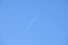 Distant Passenger Jet Plane Flying On High Altitude On Clear Blue Sky Leaving White Smoke Trace Of Contrail Behind. Air Transportation Concept