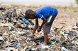 Young black boy poking aroung with a stick in a huge mountain of garbage at a landfill in West Africa