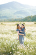 © morrowlight - Cute smiling woman holding baby girl daughter 3-4 year old wear similar dresses posing in blooming floral meadow outdoor. Mother toddler in field over nature background. Motherhood.