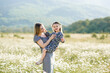 © morrowlight - Cute smiling woman holding baby girl daughter 3-4 year old wear similar dresses posing in blooming floral meadow outdoor. Mother toddler in field over nature background. Motherhood.