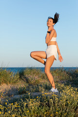 Wall Mural - happy fit woman in sportive shorts and wireless earphone jumping near blue sea.