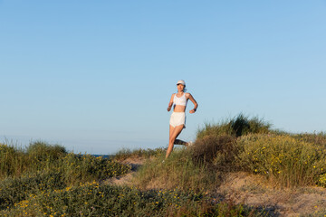 Canvas Print - young sportive woman in baseball cap and wireless earphones running on beach.