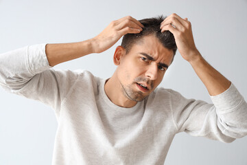 Young man with problem of dandruff on light background