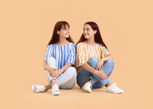 Teenage Twin Sisters Sitting On Beige Background