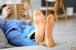 © Pixel-Shot - Young barefoot man reading book on sofa at home, closeup
