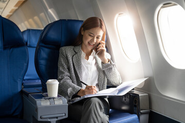 business young asian woman talking on phone during working for paperwork financial report on airplan