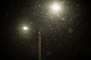 Light and snow. Lamps in dark in blizzard. Pole with two lamps.