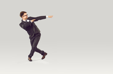 Happy smiling businessman dancing with joy and celebrating business success on gray background. Young joyful man in black suit having fun near copy space. Full length. Web banner.