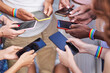 © JoseIMartin - Group of multiracial people with LGBT rainbow flag wristbands using their mobile phones. Diversity, LGBT, unity and technology concept.