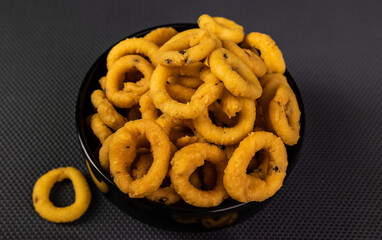 Traditional Indian snacks arranged beautifully in a black ceramic bowl with a black textured background. It is known as Chakali, Murukku, Muruku, Murkoo, Chakri.