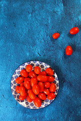 Wall Mural - Cherry tomatoes on a plate. Blue textured background with copy space.  Eating healthy concept. 